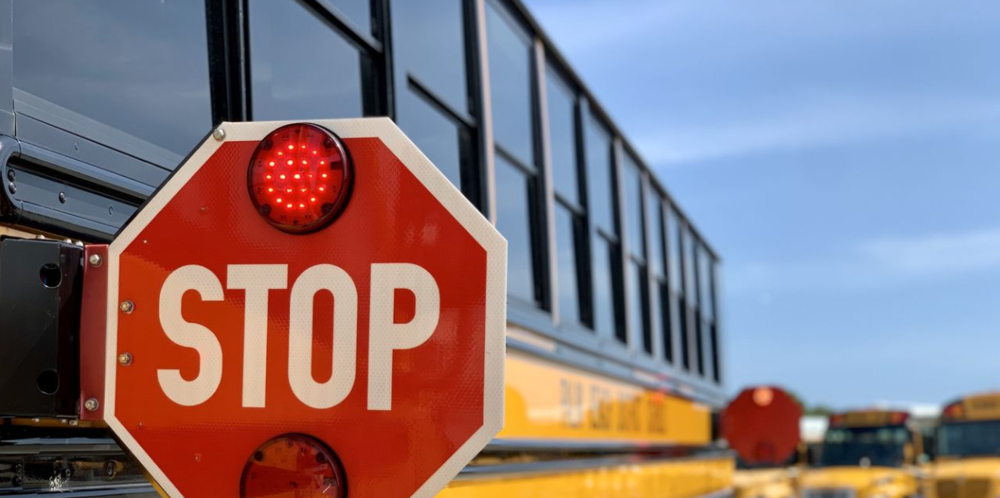 stop sign on school bus with several buses looming in the distance